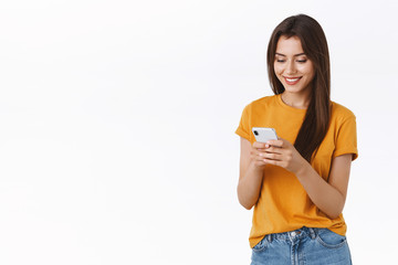 Cheerful, friendly-looking feminine woman in yellow t-shirt messaging, smiling happy and delighted, browsing internet using smartphone, shopping black friday online, place order, white background