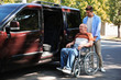© New Africa - Young man helping patient in wheelchair to get into van outdoors
