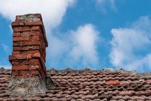 Old Red Terracotta Tile Roof With A Damaged Traditional Large Brick Chimney In Need Of Repair, On A Blue Sky Background. Home Winter Preparations.
