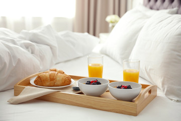 tray with tasty breakfast on bed in light room