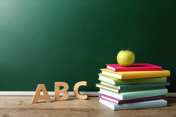 Poster - Books, letters and apple on wooden table near green chalkboard, space for text. Teacher's day