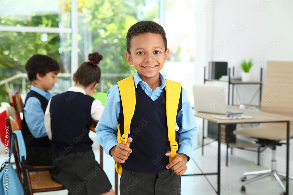 African-American boy wearing school uniform with backpack in classroom ...