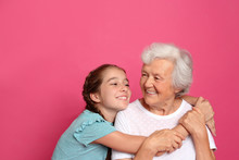 Cute Girl Hugging Her Grandmother On Pink Background