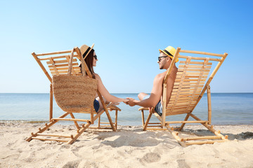 Wall Mural - Young couple relaxing in deck chairs on beach