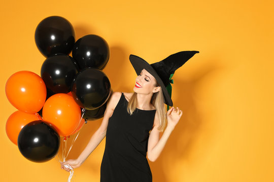 Beautiful woman wearing witch costume with balloons for Halloween party on yellow background