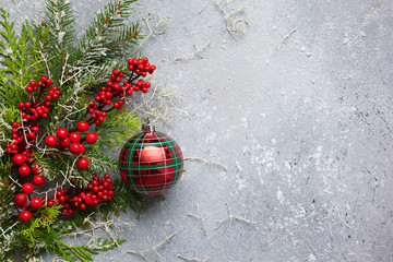 Christmas or winter background with a border of green and frosted evergreen branches, red berries and Christmas bauble on a grey vintage board. Flat lay