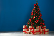 Decorated Christmas Tree And Gift Boxes Near Blue Wall. Space For Text