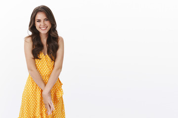 Gorgeous friendly, cheerful tender brunette girlfriend with charming toothy smile, feeling happy, laughing carefree hold hands together modest, standing yellow casual dress, white background