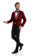 Wall Mural - happy young fashion man wearing red velvet tuxedo and presenting