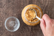 Glass jar of minced garlic and small glass bowl on wood background, woman’s hand using tablespoon to scoop out garlic