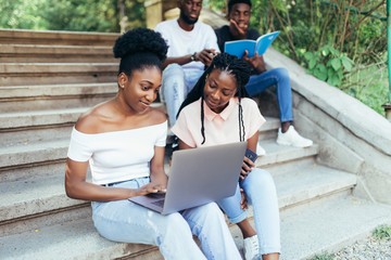 Wall Mural - Group of young african people are studying together in university. Students outdoors sitting on stairs.