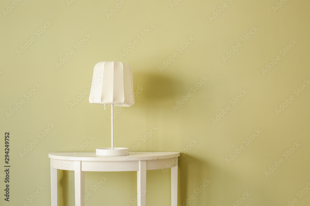 Stylish table with lamp near color wall in room