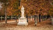 Alley of the Jardin des Tuileries covered with orange autumn leaves, statue in the Tuileries garden in Paris France on a beautiful Fall day
