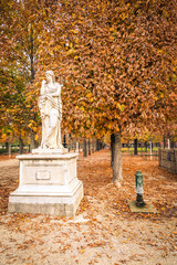 Alley of the Jardin des Tuileries covered with orange autumn leaves, statue in the Tuileries garden in Paris France on a beautiful Fall day