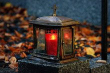Old Damaged Grave Light Made Of Metal With Burning Candle On A Grave With Autumn Leaves In Blurred Background