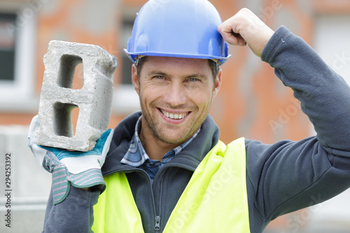 Fotomural confident handsome builder helmet carrying a cement block