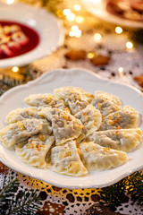 Wall Mural - Christmas dumplings stuffed with mushroom and cabbage on a white plate on a holiday table, close-up. Traditional Christmas eve dish in Poland