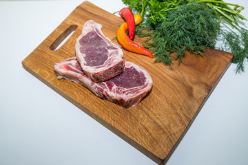 Raw beef steak with rosemary and and red hot pepper and dill on cutting board on white background.raw ribeye steak.Raw fresh Chuck roll steak with herbs and salt on a cutting Board top view.