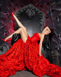 beautiful vampire woman in red long dress near big black throne in the studio