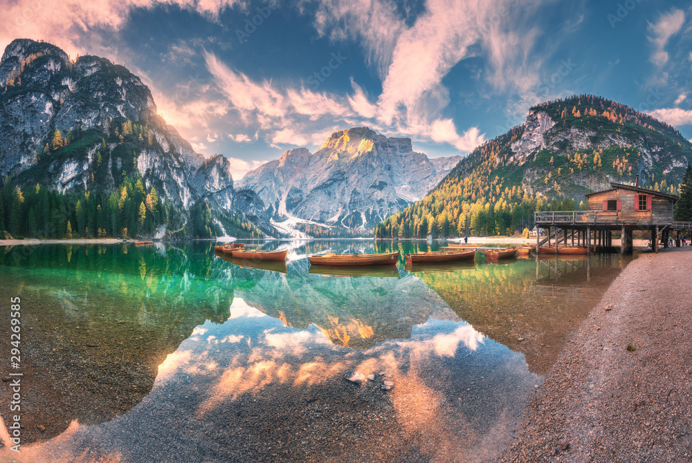 Amazing Braies lake at sunrise in autumn in Dolomites, Italy. Landscape with mountains, sky with clouds, boats, water with reflection, trees with colorful leaves. Lake in fall. Italian alps. Panorama - obrazy, fototapety, plakaty 