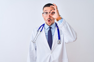 Sticker - Young doctor man wearing stethoscope over isolated background doing ok gesture shocked with surprised face, eye looking through fingers. Unbelieving expression.