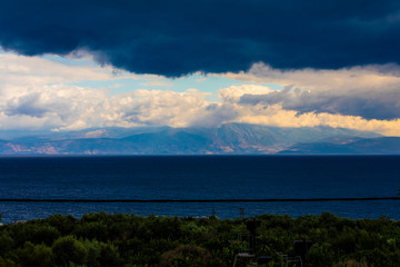 A mountain range in Greece covered in low hanging cloud with the ocean in the foreground.