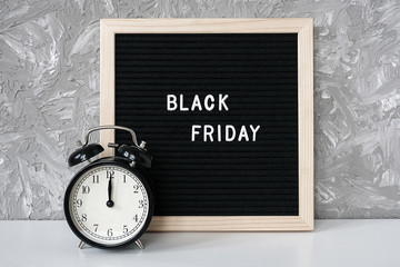 Text Black friday on black letter board and alarm clock on table against grey stone background. Concept Black friday , season sales time
