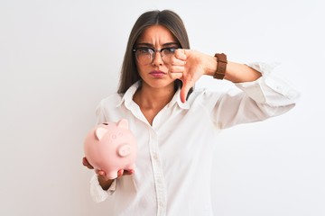 Wall Mural - Beautiful businesswoman wearing glasses holding piggy bank over isolated white background with angry face, negative sign showing dislike with thumbs down, rejection concept
