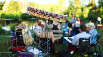 Wall Mural - Sacred drums at spiritual singing group. Blurred people are seen in a singing circle at a local park during a sunny afternoon, details on the side of a handmade native drum are seen in the foreground.