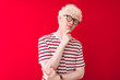 © Krakenimages.com - Young albino blond man wearing striped t-shirt and glasses over isolated red background with hand on chin thinking about question, pensive expression. Smiling with thoughtful face. Doubt concept.