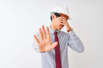 Wall Mural - Chinese architect man wearing tie and helmet standing over isolated white background covering eyes with hands and doing stop gesture with sad and fear expression. Embarrassed and negative concept.