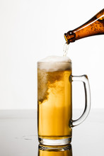 Beer Pouring From Bottle Into Glass With Bubbles Isolated On White