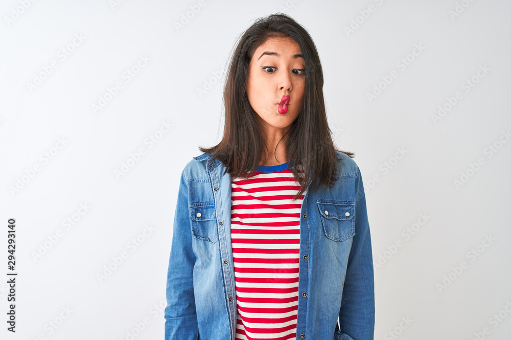 Young chinese woman wearing striped t-shirt and denim shirt over isolated white background making fish face with lips, crazy and comical gesture. Funny expression.