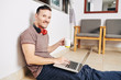 © DragonImages - Happy young man in comfy casual clothes drinking another cup of coffee when working on laptop on the floor in his room
