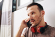 © DragonImages - Serious Caucasian young man with headphones around his neck answering important phone call