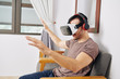 © DragonImages - Smiling young man in virtual reality headset and headphones playing videogame at home