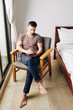 © DragonImages - Serious pensive young man sitting in armchair next to his bed and writing plans for the day
