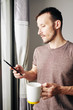 © DragonImages - Smiling attractive young man in casual t-shirt holding big cup of tea and reading text messages from friends and colleagues