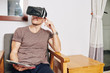 © DragonImages - Man with tablet computer in hands using virtual reality headset when sitting on chair at home