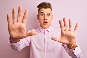 Young handsome businessman wearing elegant shirt standing over isolated pink background afraid and terrified with fear expression stop gesture with hands, shouting in shock. Panic concept.