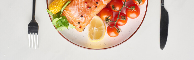 top view of raw salmon steak with vegetables on plate near cutlery on marble table, panoramic shot