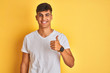 © Krakenimages.com - Young indian man wearing white t-shirt standing over isolated yellow background doing happy thumbs up gesture with hand. Approving expression looking at the camera showing success.