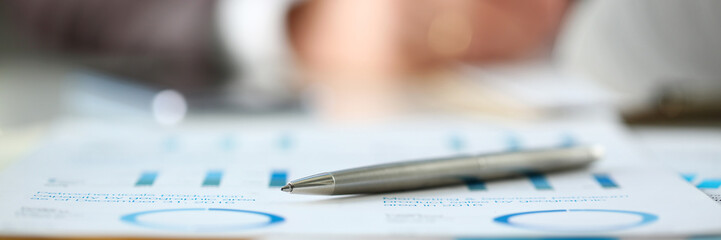 Wall Mural - Silver pen lie at important paper on table in office closeup with businessman in background. Paperwork job trade balance bank credit loan money invest payment irs commerce partnership concept