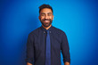 © Krakenimages.com - Young indian businessman wearing elegant shirt and tie standing over isolated blue background with a happy and cool smile on face. Lucky person.