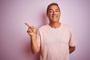 Wall Mural - Handsome middle age man wearing t-shirt standing over isolated pink background with a big smile on face, pointing with hand and finger to the side looking at the camera.