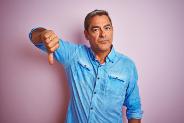 Handsome middle age man wearing blue denim shirt standing over isolated pink background with angry face, negative sign showing dislike with thumbs down, rejection concept