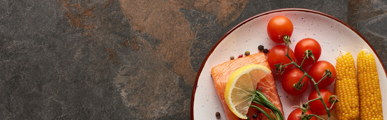 panoramic shot of raw salmon steak with tomatoes, corn, lemon, rosemary and pepper on plate