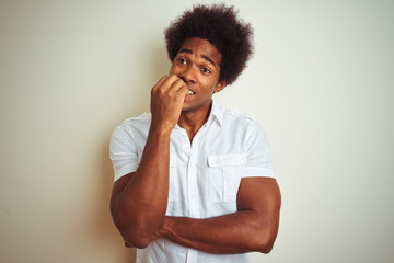 Poster - African american man with afro hair wearing shirt standing over isolated white background looking stressed and nervous with hands on mouth biting nails. Anxiety problem.