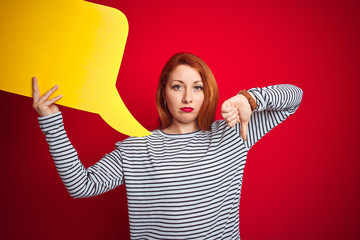 Sticker - Young beautiful redhead woman holding yellow speech bubble over red isolated background with angry face, negative sign showing dislike with thumbs down, rejection concept