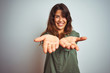 © Krakenimages.com - Young beautiful woman wearing green shirt standing over grey isolated background Smiling with hands palms together receiving or giving gesture. Hold and protection